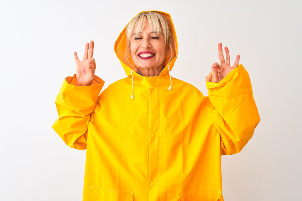 中年妇女穿着雨衣和兜帽站在孤立的白色背景放松和微笑，闭上眼睛做冥想手势与手指。瑜伽的概念。图片下载
