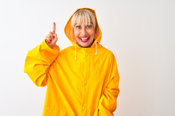 中年妇女穿着雨衣与兜帽站在孤立的白色背景指向手指与成功的想法。退出和快乐。第一。图片下载