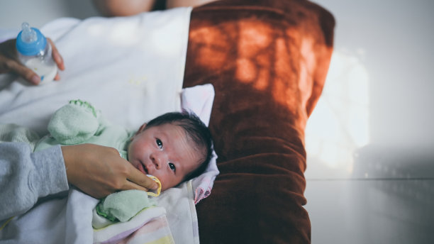 年轻母亲在舒适的尿布床上用奶瓶喂完奶后给宝宝擦嘴的照片图片下载
