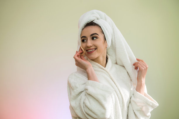 淋浴后穿着浴袍和毛巾的年轻漂亮女人正在化妆，往脸上扑粉图片下载