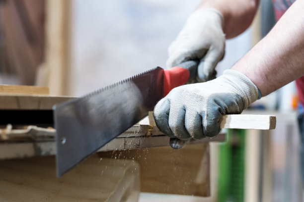 木匠男，戴着特殊手套，用手锯工作。图片下载