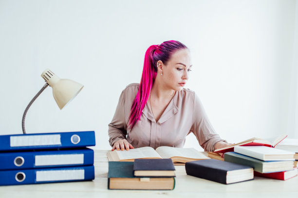 粉红色头发的女商人坐在办公室里读教育书籍图片下载