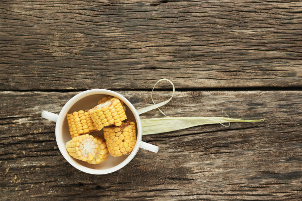 碗里的玉米，还有笔。耳朵被切成四段。用旧木板做成的桌子上放着白色盘子。俯视图，水平方向图片下载
