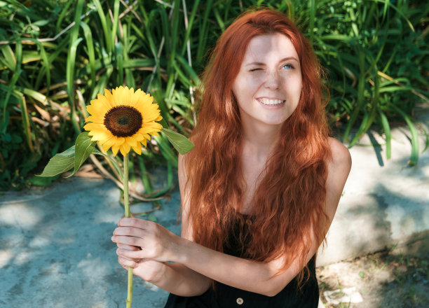 可爱的姜黄色女孩与向日葵在公园。图片下载