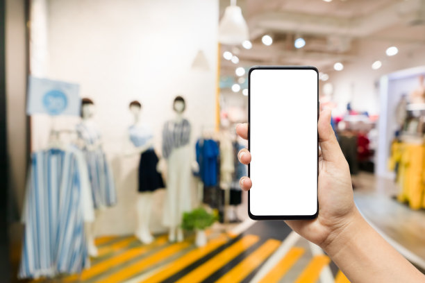 在女装店手持智能手机。手机模型图，手持空白白色屏幕智能手机，用于在女装时尚店的模糊抽象背景上进行广告宣传。图片下载