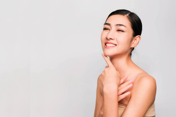 年轻美丽的亚洲女人与干净和明亮的皮肤，化妆品美丽的概念，手触摸脸颊，微笑和友好的脸孤立在灰色的背景图片下载