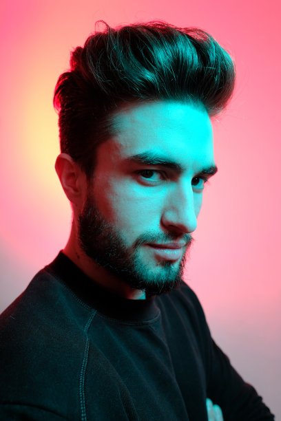 在时尚霓虹灯下的工作室里摆姿势的年轻英俊模特，鲜艳的色彩，明亮的光效，迪斯科风格。图片下载