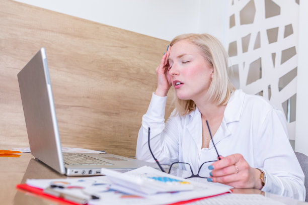 感觉筋疲力尽。沮丧的年轻女子看起来筋疲力尽，而坐在她的工作地点，拿着她的眼镜图片下载