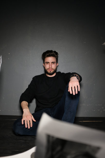 一个留着胡须的年轻黑发男子坐在地板上，将文件扔向空中，表达人类情感图片下载