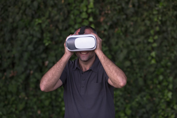 年轻人享受虚拟现实眼镜耳机或3d眼镜在绿色常春藤的背景。在户外。技术、创新、网络空间和游戏。图片下载