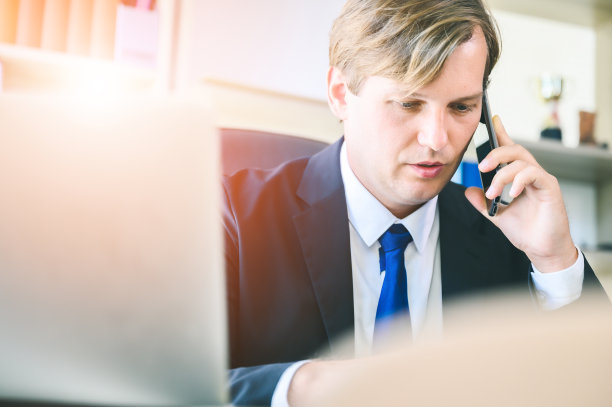 年轻的商人在办公室里忙着工作。他用手机和他的合作伙伴谈论他的生意图片下载