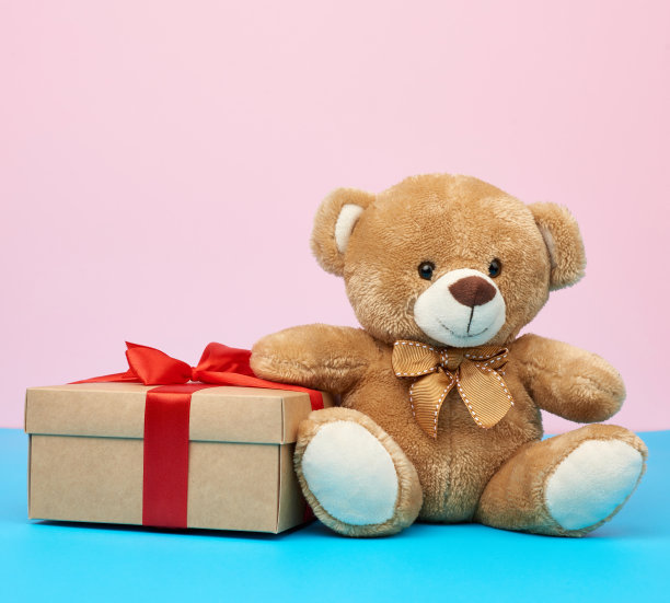 可爱的棕色小泰迪熊拿着一个棕色的盒子，盒子上有一条红丝带图片下载