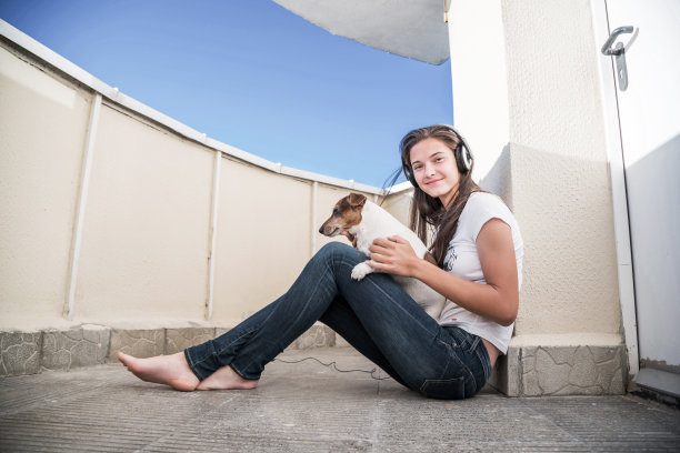 穿着牛仔裤的女孩戴着耳机和狗坐在阳台上图片下载