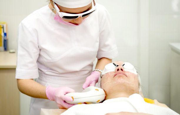 医生给病人涂一种特殊的凝胶。专业设备抗痤疮光疗。美丽的女人在照片复原程序。美容诊所面部皮肤治疗。图片下载