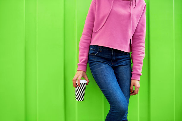 穿着粉色运动衫的年轻女人拿着咖啡的局部照片，女学生在绿色墙壁背景下喝热饮图片下载