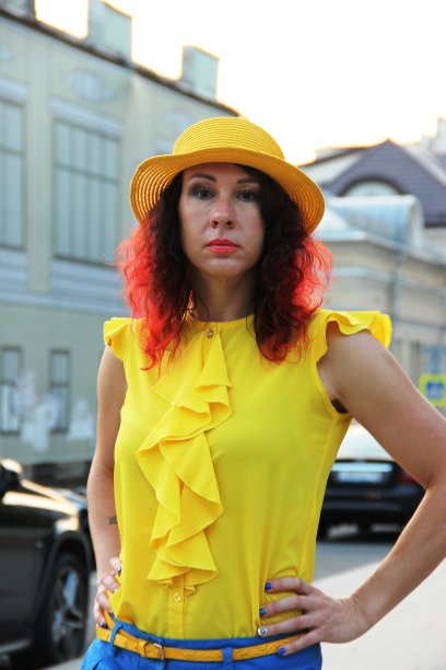 一个女人在夜晚的街道上微笑。一个留着红色卷发，穿着黄色丝绸衬衫，戴着黄色帽子的女人。城市环境中的肖像图片下载