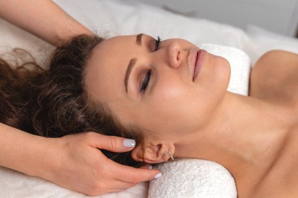 可爱的年轻女孩闭上眼睛，浓眉和完美的皮肤在头部按摩，女人放松在白色毛巾的背景，美容照片概念的皮肤护理和水疗治疗，侧视图图片下载