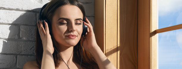 一个漂亮的女孩在阳光下享受着音乐旁边的窗户的广角镜头图片下载