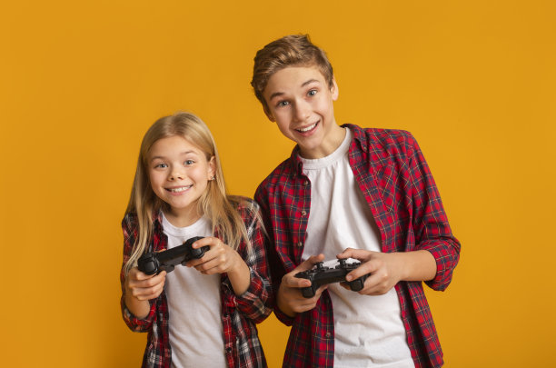 儿童休闲：兄妹在黄色背景下手持游戏手柄图片下载