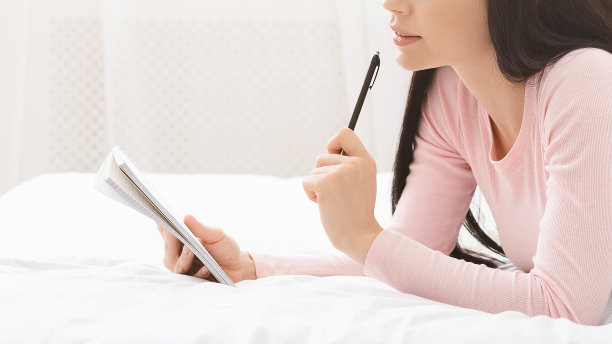 在床上思考的梦幻女孩，手持笔和笔记本图片下载