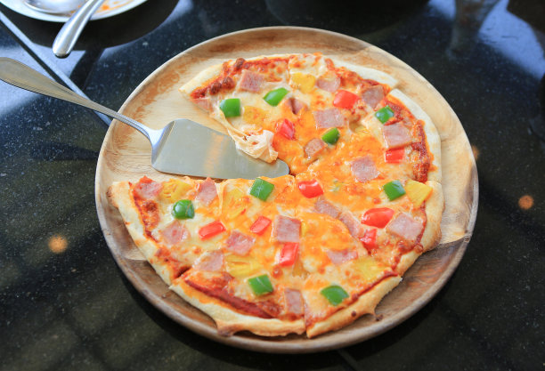 披萨放在木托盘上，靠在黑色的桌子上。夏威夷风格。图片下载