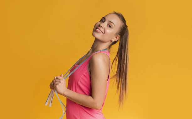 手持跳绳在黄色背景前摆姿势的阳光运动女性图片下载