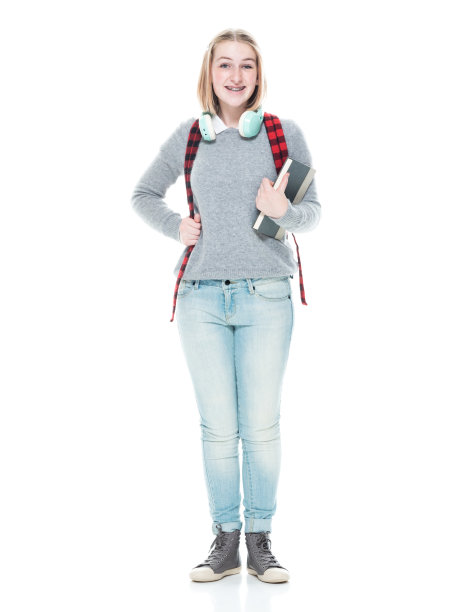 十几岁的女高中生穿着polo衫，拿着课本，戴着耳机站在白色背景前图片下载