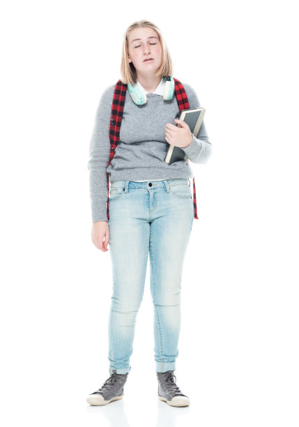 十几岁的女高中生穿着polo衫，拿着课本，戴着耳机站在白色背景前图片下载