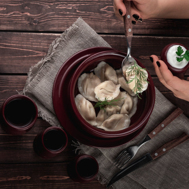 女手里拿着一个勺子用自制的饺子，红锅里有酱汁，饮料在深色的木质背景上用麻布包着，民族美食概念为餐厅的菜单，方形照片图片下载