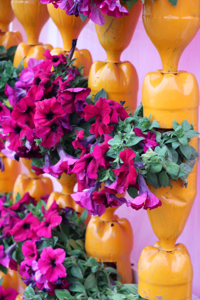 垂直花园的形象使用回收的塑料苏打瓶作为花盆，升级的瓶子填满土壤和植物，漆成黄色并组装成柱设计，环保和节省空间的花园设计理念图片下载