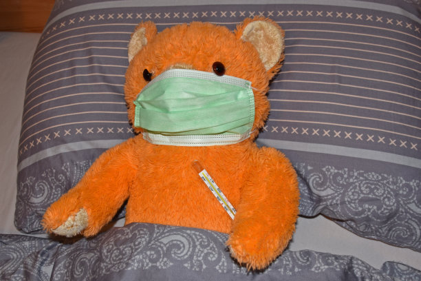 橙色的泰迪熊躺在床上，带着体温计和流感口罩图片下载