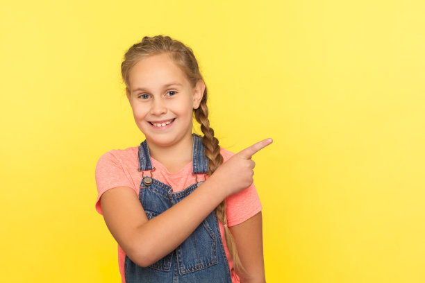 看,在这里做广告!活泼可爱的小女孩的肖像在牛仔工装裤指向侧拷贝空间图片下载