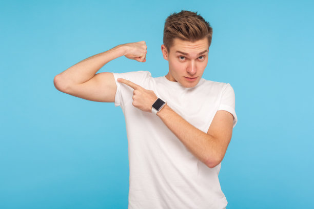 看我的力量!一幅穿着白色t恤的身材苗条的年轻人的肖像，指着二头肌，举起的手上露出肌肉图片下载