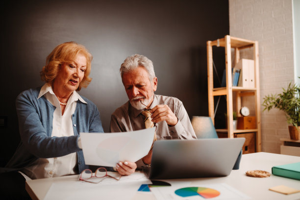 老年金发女人和灰发男人在办公桌旁看图表照片特写图片下载