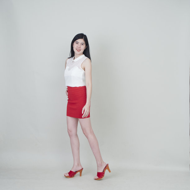 美丽的女人穿着红色短裙在灰色的墙壁工作室拍摄。图片下载