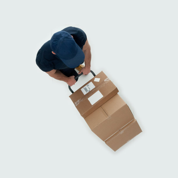 白人年轻男性送货员，戴着便帽，拿着箱子，开着手推车，走在白色背景的送货车前图片下载