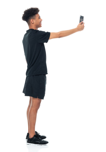 非裔美国青年男性穿着短裤，站在白色背景前用手机拍照图片下载