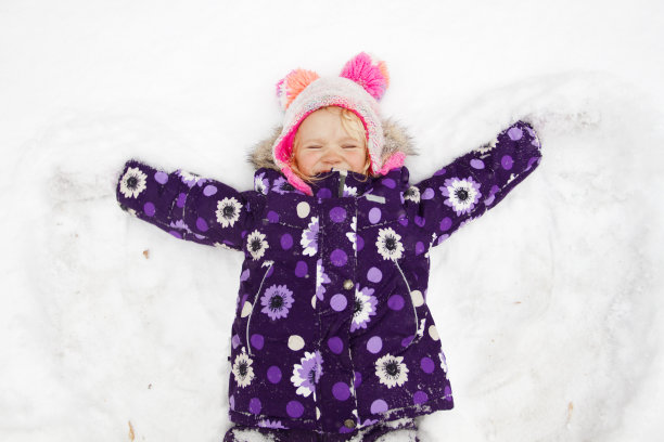 可爱的蹒跚学步的女孩在寒冷的冬天在户外做雪天使图片下载