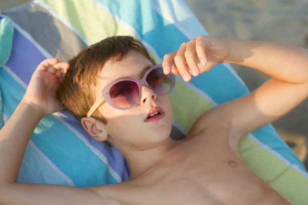 在一个美丽的夏日，一个小男孩戴着太阳眼镜躺在太阳床上图片下载
