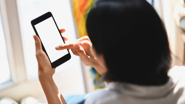 女艺术家坐在木地板上，手持白色空白屏幕智能手机的局部照片图片下载