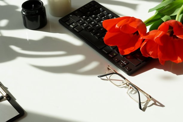 女士的办公桌上有笔记本电脑，春天的鲜花，红色的郁金香，饰品，口红上的光背景与太阳的阴影俯视图。节日、情人节、妇女节的背景。副本的空间。图片下载