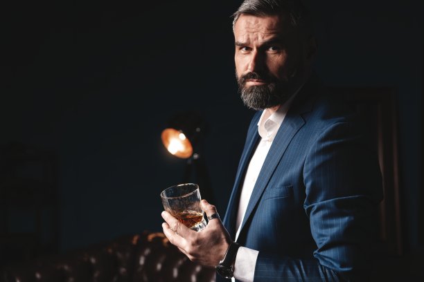 品尝品尝。有胡子的男人拿着一杯白兰地。品尝和品尝概念。穿着优雅西装的大胡子商人，端着一杯威士忌图片下载