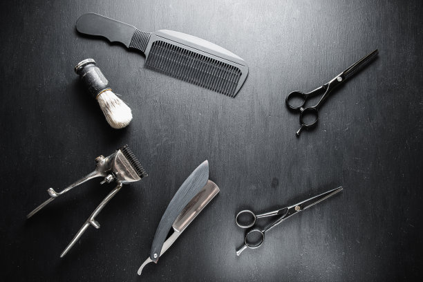 在布满灰尘的黑色表面上是旧的理发工具。老式手工理发器、梳子、剃须刀、剃须刷、剃须刷、美容剪刀。黑色的单色。图片下载