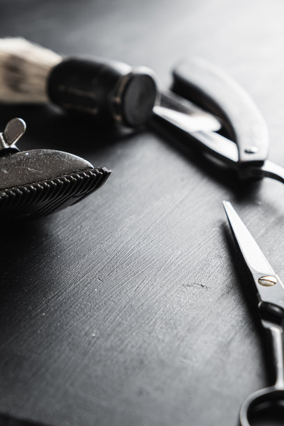 在布满灰尘的黑色表面上是旧的理发工具。老式手工理发器、梳子、剃须刀、剃须刷、剃须刷、美容剪刀。黑色的单色。垂直图片下载