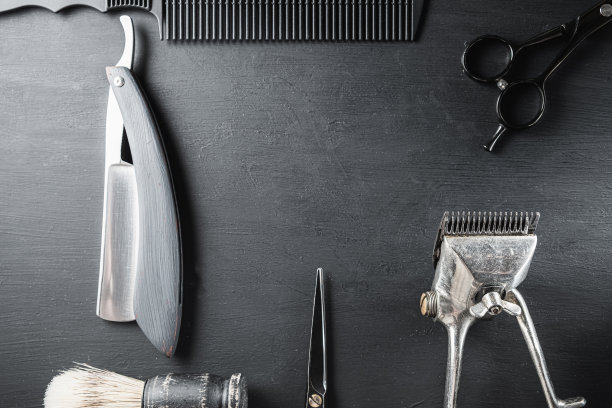 在布满灰尘的黑色表面上是旧的理发工具。老式手工理发器、梳子、剃须刀、剃须刷、剃须刷、美容剪刀。黑色的单色。图片下载