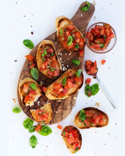 切菜板和白色木桌上放着番茄和罗勒烤面包，平铺，特写。传统的意大利素食小吃图片下载