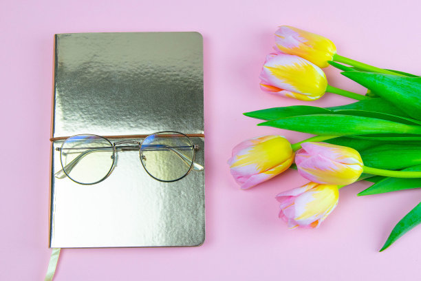 彩色大头针和黄色郁金香与笔记本和眼镜平躺孤立的大头针背景俯视图。春天的花。妇女节、母亲节庆祝。网络旗帜模板。库存图片图片下载