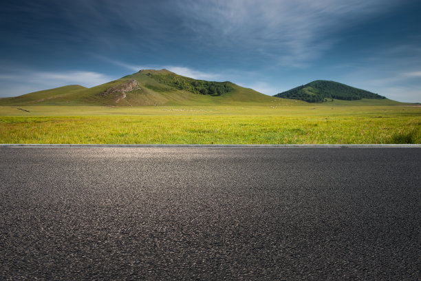 春天一望无际的草原和远处柏油公路旁的山林图片下载