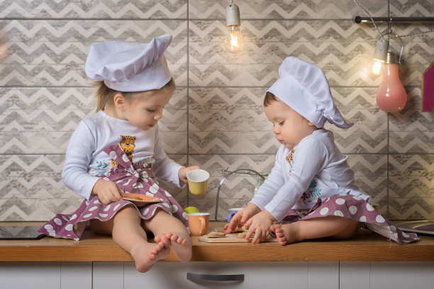 两个小厨师。姐妹们在厨房帮忙准备食物后感到累了，她们正坐在厨房的桌子上喝茶，饼干。图片下载