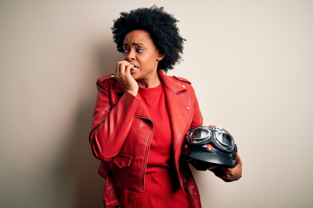 拿着摩托车头盔，看起来紧张焦虑的年轻非裔美国摩托车手图片下载